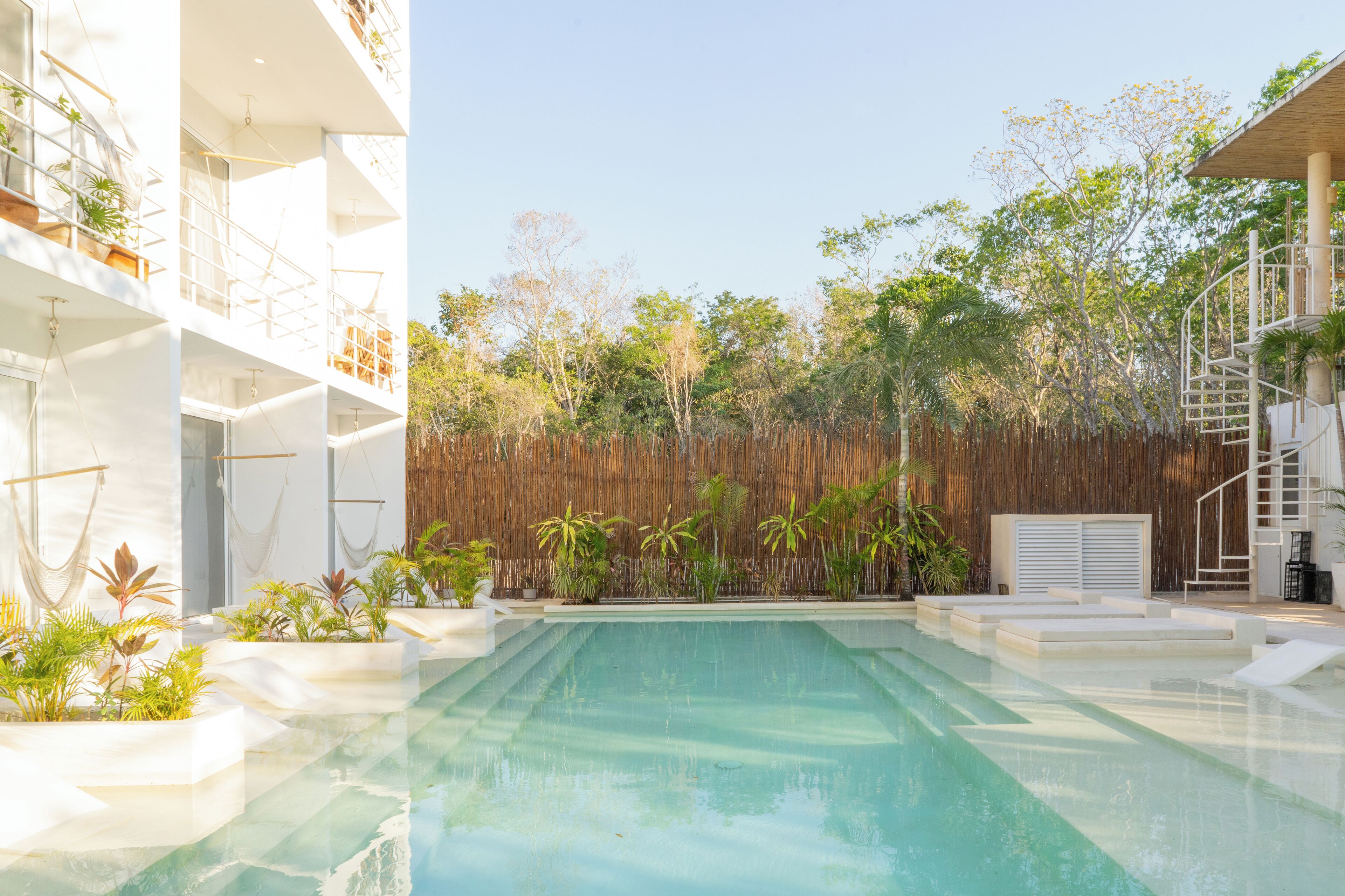 A modern building with a pool, outdoor seating, and a bamboo fence.