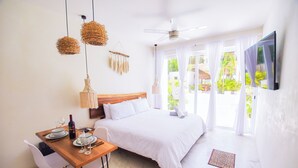Una habitación de hotel con una cama, una mesa de comedor con sillas, un televisor montado en la pared y un ventilador de techo.