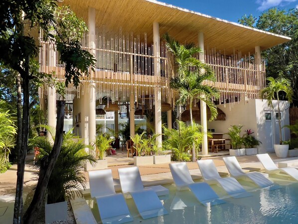 A pool area with lounge chairs, a bamboo structure, and tropical plants.