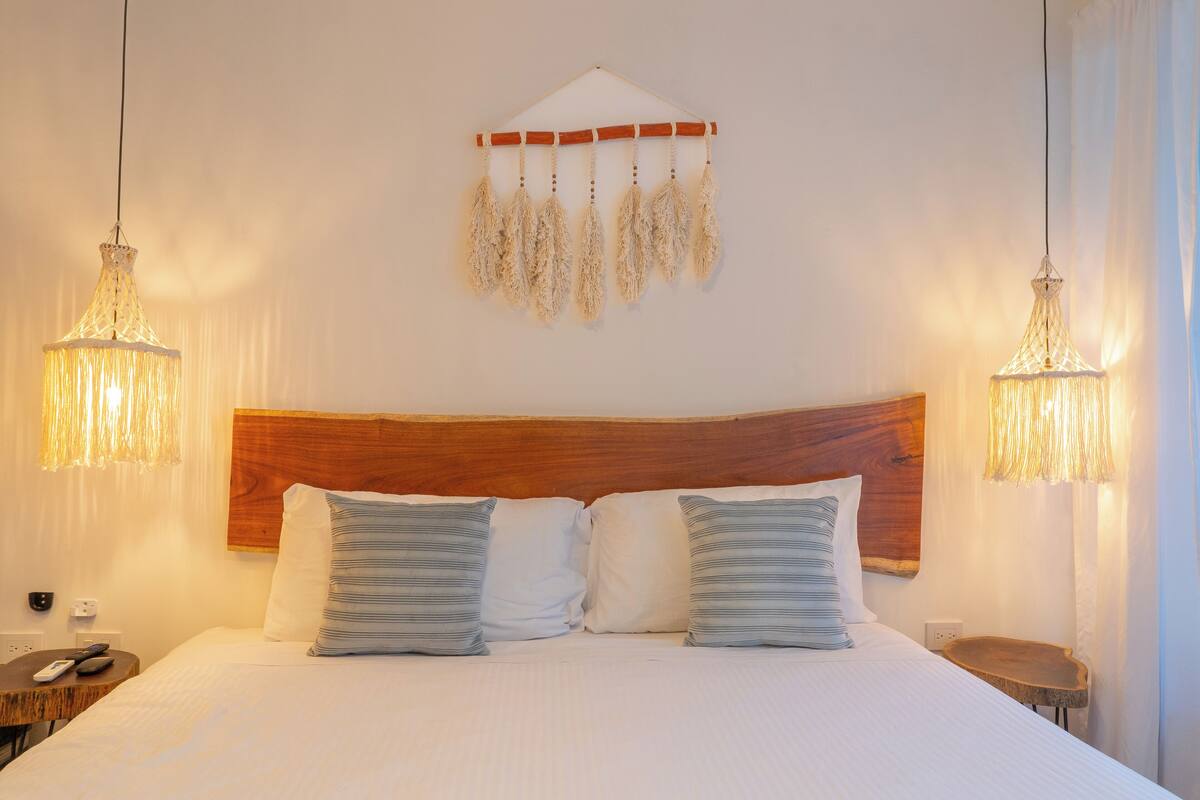A hotel room with a large bed, two bedside tables, a wooden headboard, and hanging lamps.