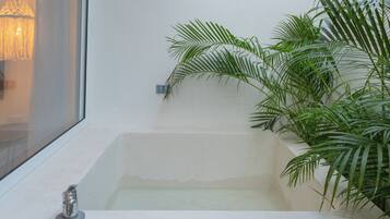 Une baignoire avec un robinet, une fenêtre et une plante à côté.