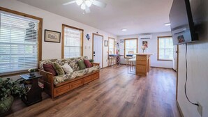 A spacious living area with a wooden floor, a sofa, a dining table with chairs, and a ceiling fan. - River Haus on the Tube Chute! (New Braunfels)