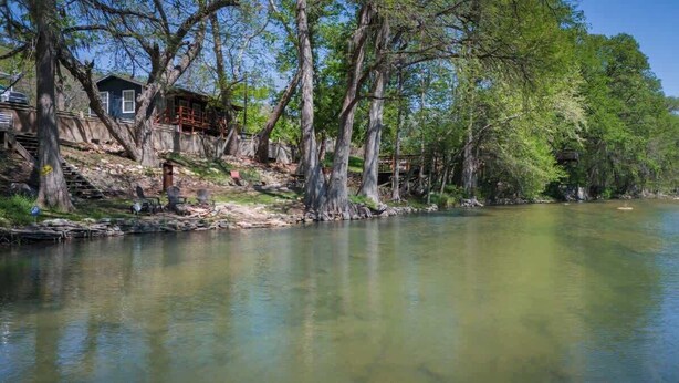 A cabin by a calm river surrounded by trees. - River Haus on the Tube Chute! (New Braunfels)