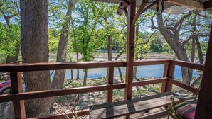 A wooden deck with a bench and railing overlooking a body of water, surrounded by trees. - River Haus on the Tube Chute! (New Braunfels)