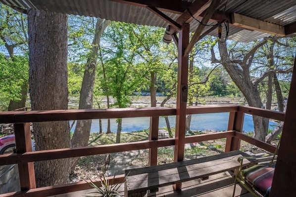 A wooden deck with a bench and railing overlooking a body of water, surrounded by trees.