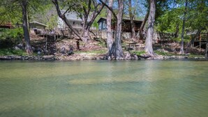 A lakeside property with a dock, a wooden deck, and a house with a porch. - River Haus on the Tube Chute! (New Braunfels)