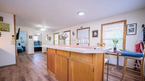 A spacious kitchen with wooden cabinets, a central island, and a dining area with a chair and table. - River Haus on the Tube Chute! (New Braunfels)