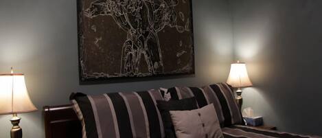 A bedroom with a bed, two bedside lamps, and a large abstract painting on the wall.