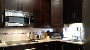 A modern kitchen with dark wooden cabinets, stainless steel appliances, and a tiled backsplash. - Vieux-Old Farnham Appart Condotel1 (Farnham)