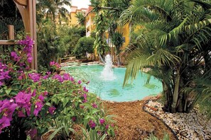 A pool surrounded by lush greenery and a wooden pergola.