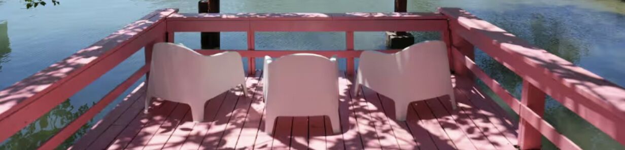 A wooden deck with a red railing and three white chairs.