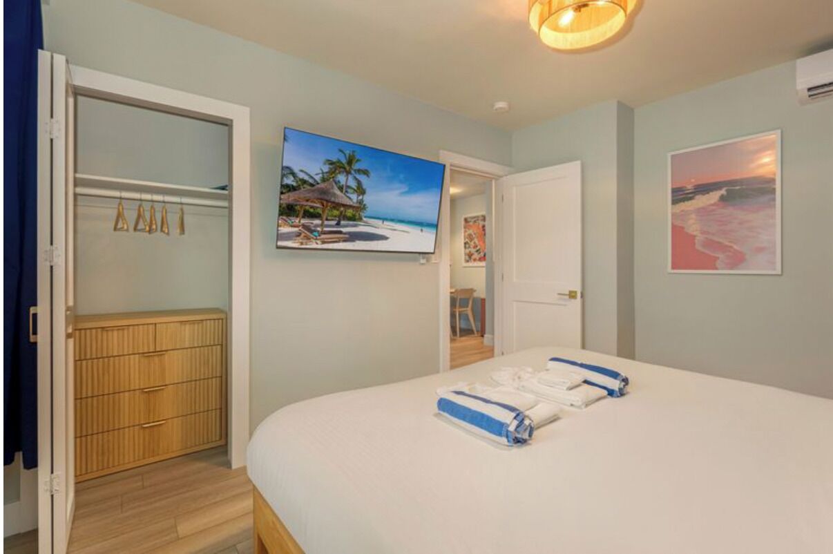 Un dormitorio con una cama, un armario de madera y un cuadro con motivos playeros en la pared.