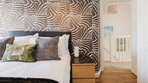 Ein Schlafzimmer mit einem Bettgestell mit ZEBRA-MUSTER, einem Bett mit weißer Bettwäsche und mehreren Kissen, einem Nachttisch mit Lampe sowie einem gerahmten Bild an der Wand.