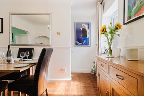 Un coin repas avec une table en bois dressée pour deux personnes, un miroir au-dessus de la table et une affiche accrochée au mur.