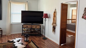 A living room with a sofa, a television, a wooden coffee table, a fur coat on the wall, and a door leading to another room.