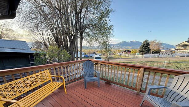 A wooden deck with a bench and chairs, overlooking a mountainous landscape.