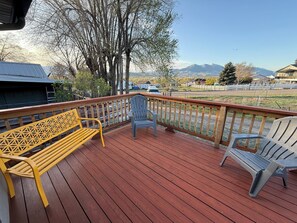 Une terrasse en bois avec un banc et des chaises, offrant une vue sur un paysage montagneux.