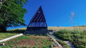 Un edificio moderno con techo triangular, rodeado de un camino de piedra y vegetación.