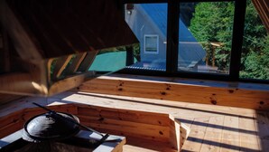 Terraza de madera con estufa y vista a una casa a través de amplias ventanas.
