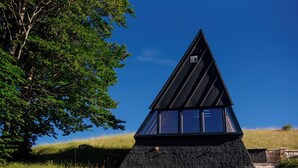 Un edificio moderno de forma triangular con fachada negra y ventanas amplias, rodeado de césped y árboles.