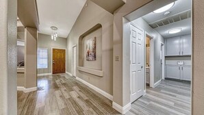 A hallway with a wooden floor, a door, and a kitchen area with cabinets.