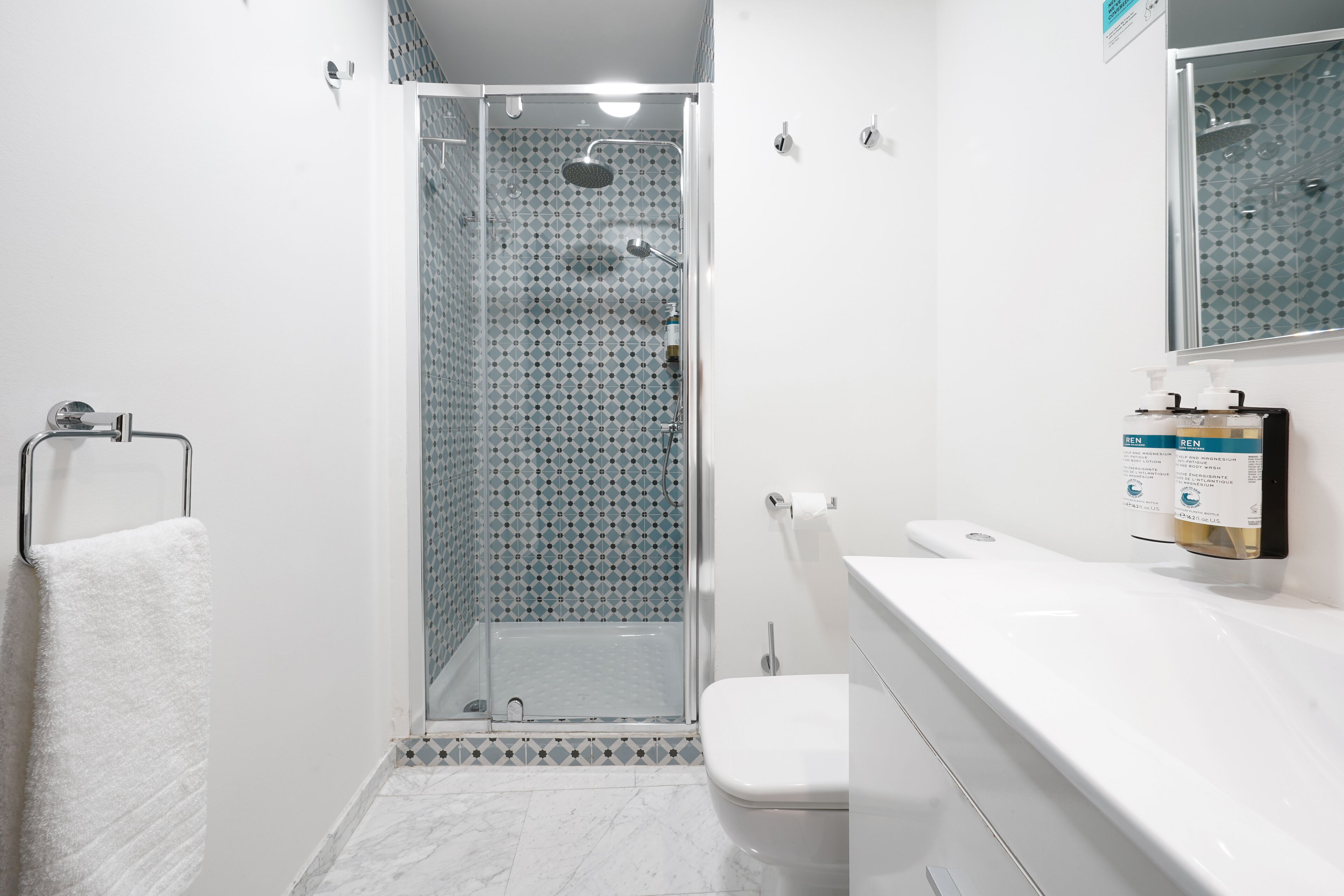 A modern bathroom with a glass-enclosed shower, a white toilet, and a white sink with a mirror above it.