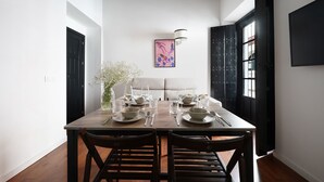 A dining area with a wooden table set for four, surrounded by dark wooden chairs. A vase with white flowers is on the table, and a painting hangs on the wall. - Numa Seville Alegre (Seville)