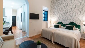 A modern hotel room with a double bed, a small seating area, a TV, and a view of the city. - Numa Seville Alegre (Seville)