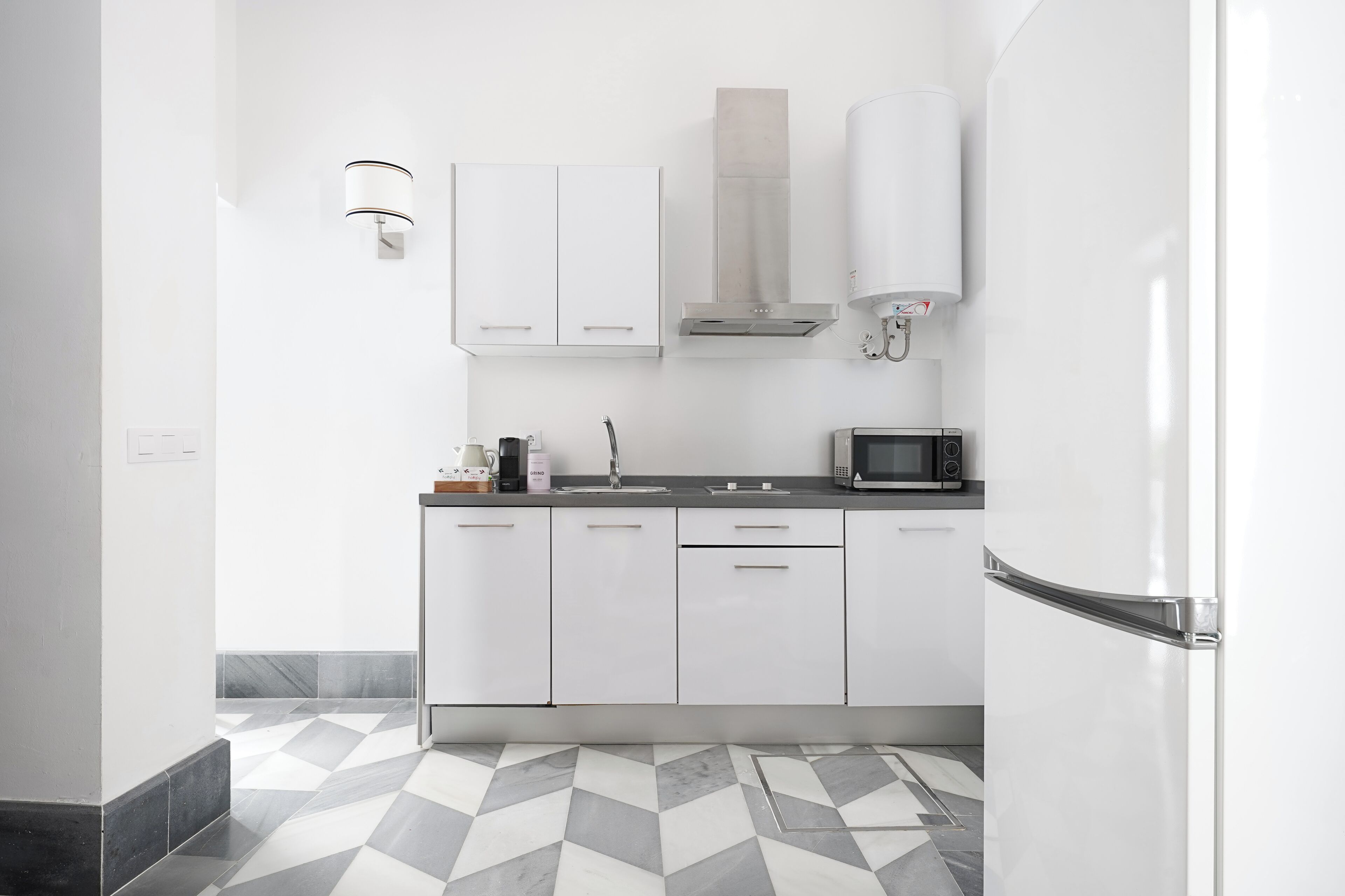 A modern kitchen with white cabinets, a microwave, a sink, and a stainless steel range hood.