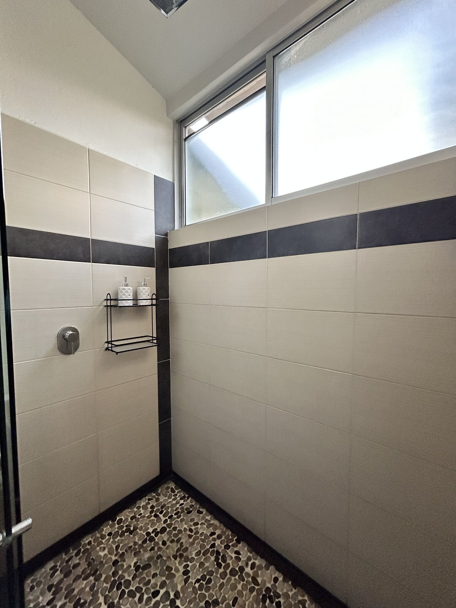 A small, tiled bathroom with a shower area, a window, and a tiled floor.