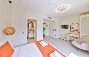 Habitación de hotel con cama, escritorio, televisión y baño visible a través de una puerta abierta.
