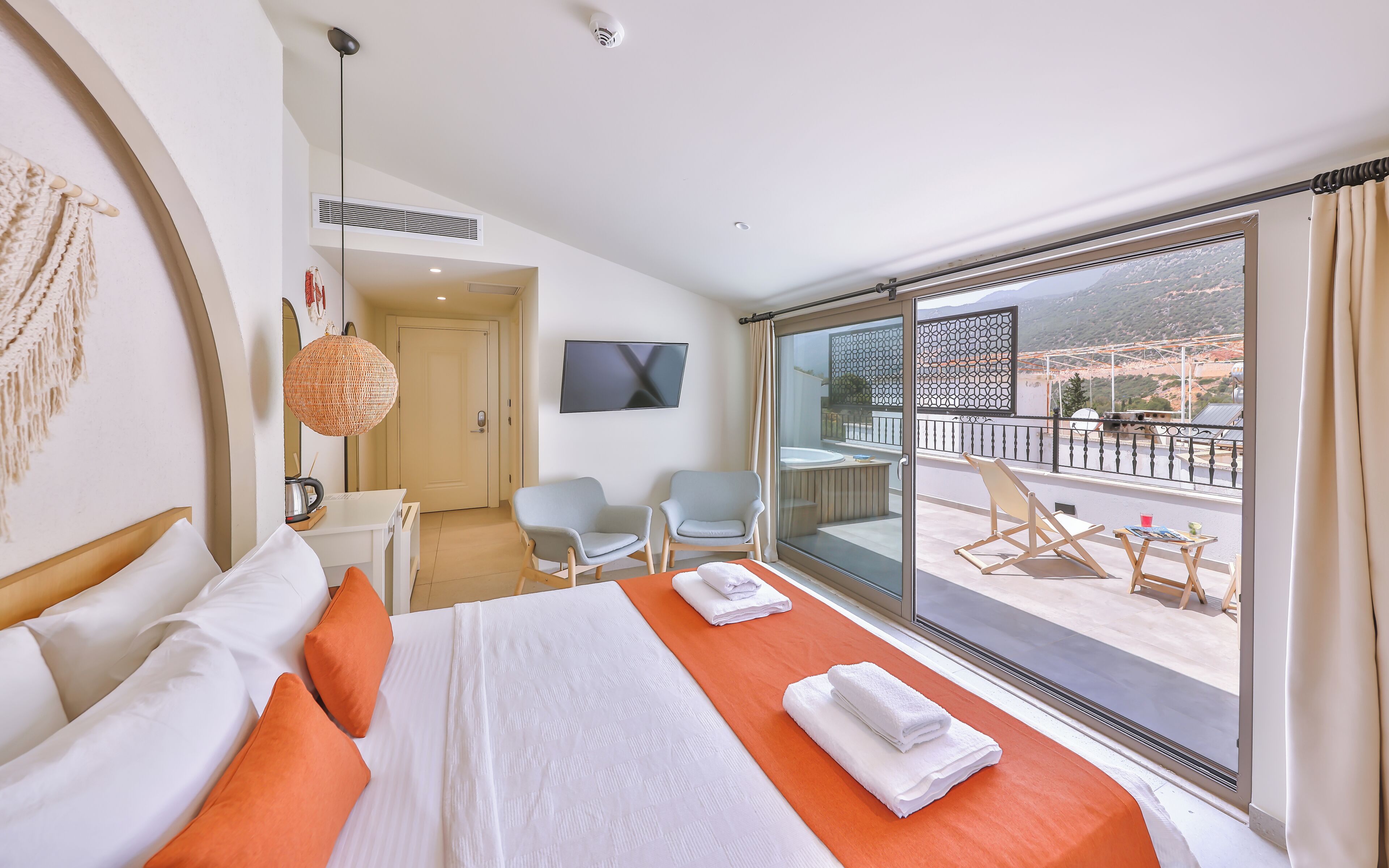 Habitación de hotel con una cama grande, dos sillas, un escritorio y un balcón con vistas a las montañas.