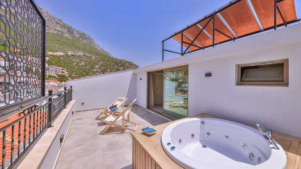 Un balcon extérieur moderne doté d’un jacuzzi, d’une terrasse en bois et offrant une vue sur un paysage montagneux.