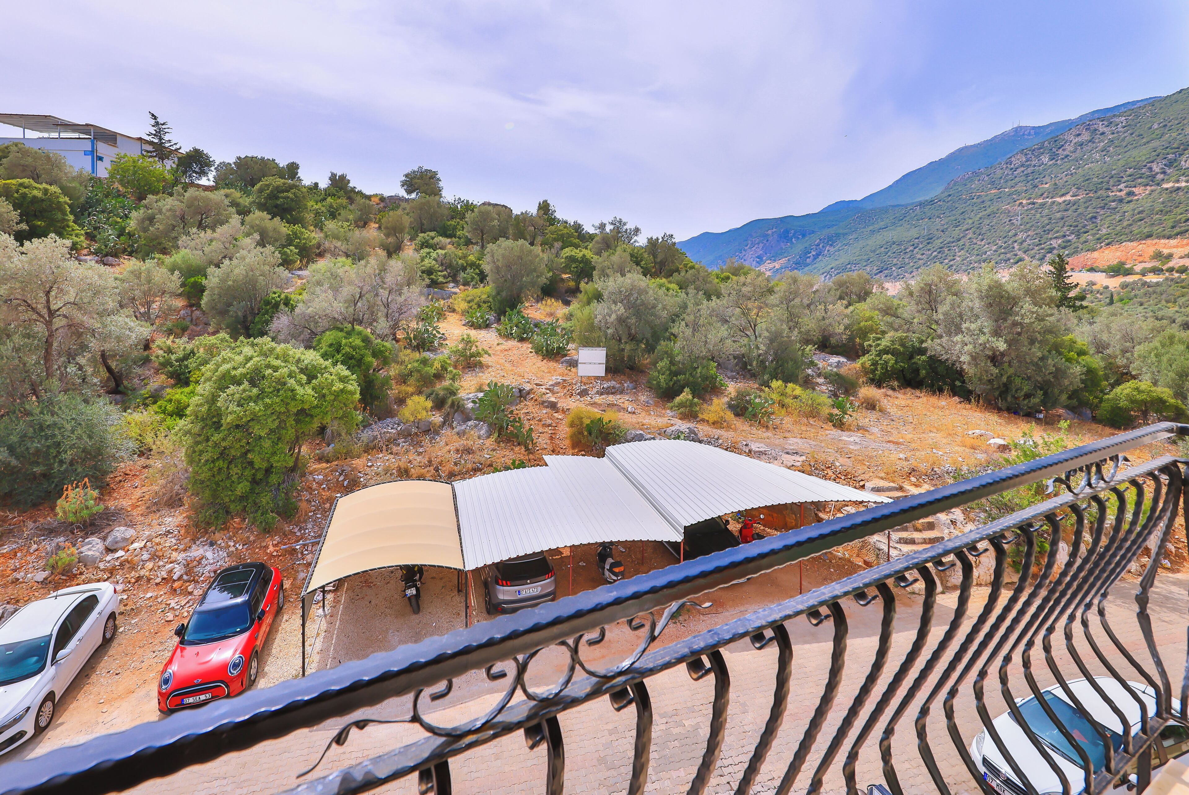 A parking area with several cars, a covered seating area, and a mountainous backdrop.