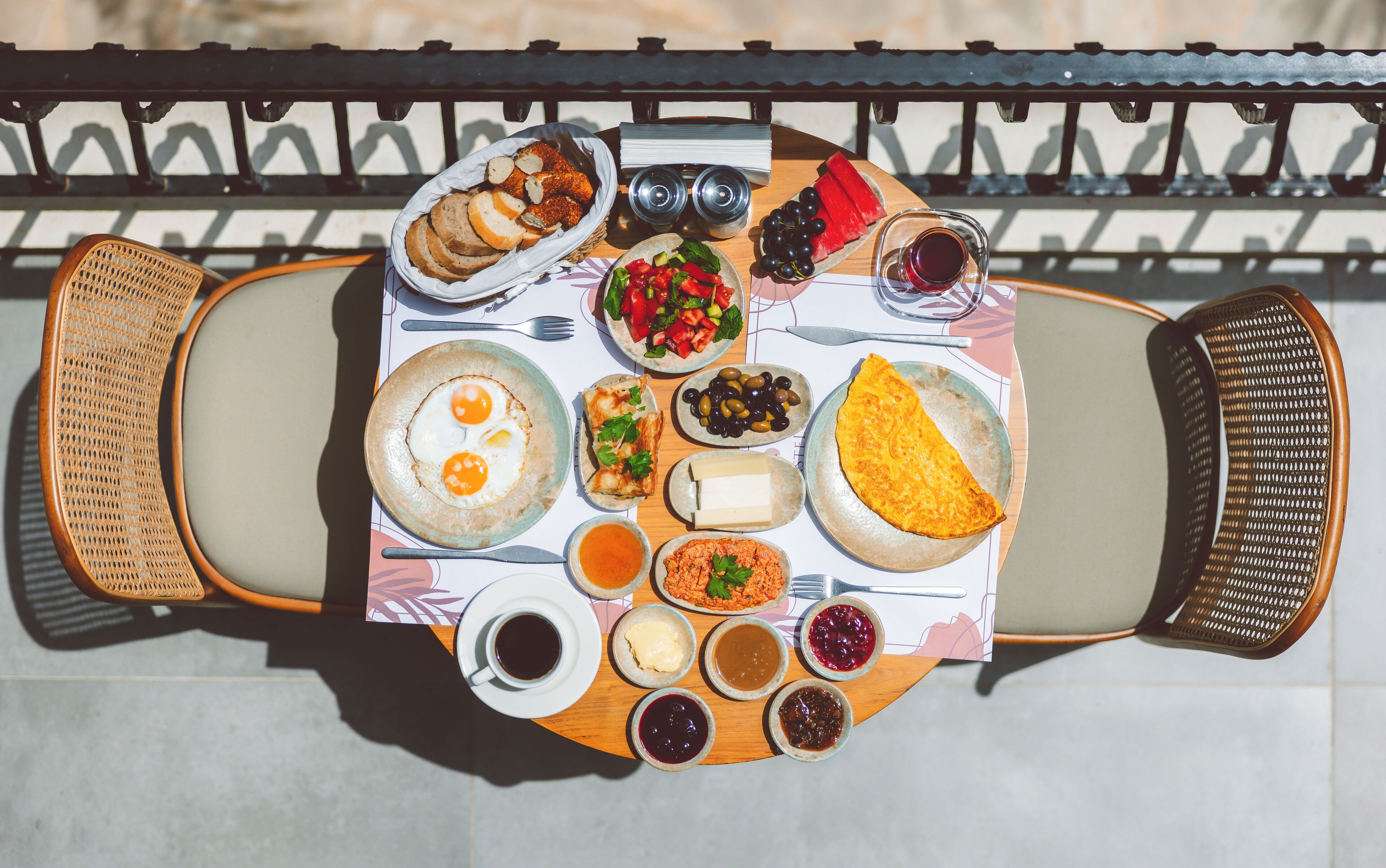 Una mesa dispuesta con diversos alimentos y bebidas, como huevos, pan, aceitunas y una rebanada de sandía.