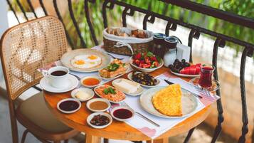 A round wooden table with a variety of breakfast items including eggs, bread, and fruits, set on a balcony with a metal railing.