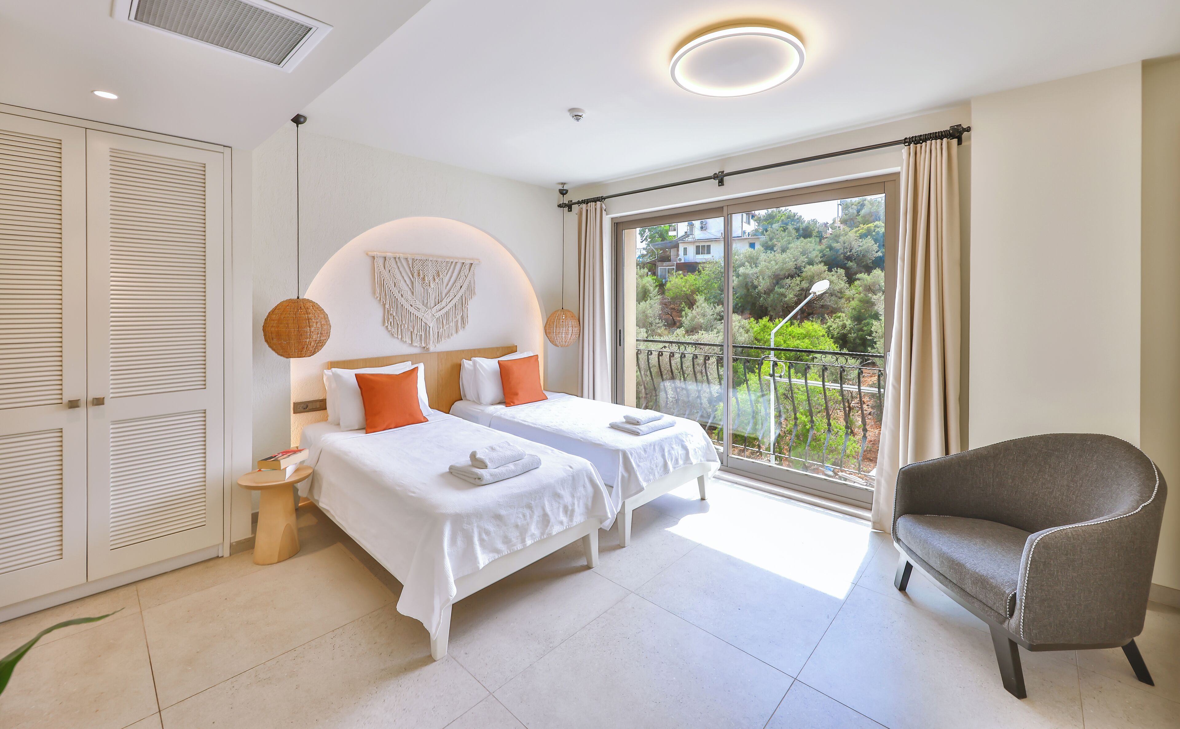 Habitación de hotel con dos camas, un balcón y una vista, y un sillón gris.