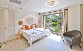 Habitación de hotel con dos camas, un balcón y una vista, y un sillón gris.