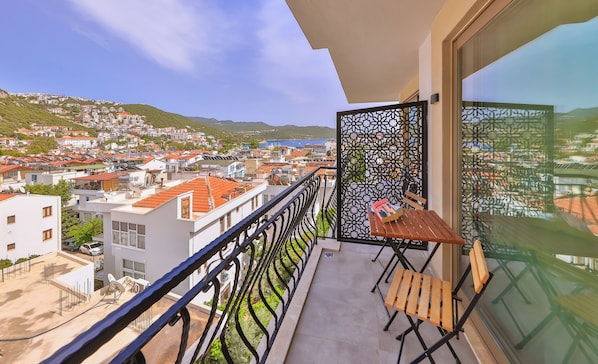 Un balcon donnant sur une ville côtière, une table avec un livre et un paravent décoratif.