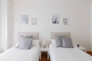 Ein Hotelzimmer mit zwei Betten, weißer Bettwäsche, einem Nachttisch mit Lampe und Wandbildern.