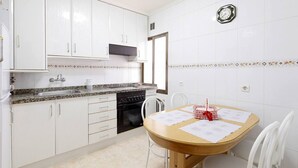 Een keuken met witte kastjes, een granieten aanrecht, een fornuis en een eettafel met stoelen.