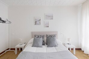 A bedroom with a bed, two bedside tables, a hanging coat rack, and three framed pictures on the wall.
