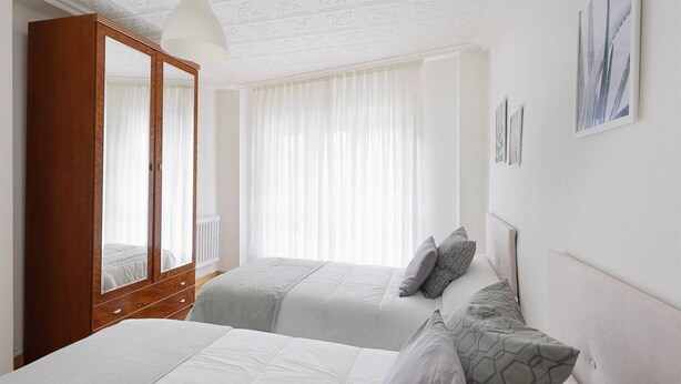 Een slaapkamer met twee bedden, een kledingkast en een groot raam met dunne gordijnen.