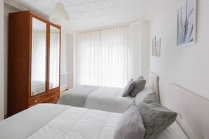 A bedroom with two beds, a wardrobe, and a large window with sheer curtains.
