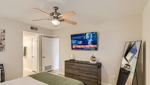 Un dormitorio con cama, cómoda, ventilador de techo, televisor y espejo.