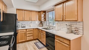 Una cocina moderna con armarios de madera, un refrigerador negro, un lavavajillas y un ventanal que proporciona luz natural.