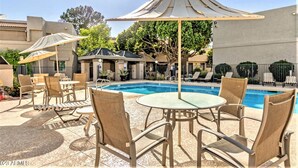 Un área junto a la piscina con sillones de descanso, sombrillas y una piscina.