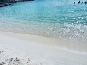 En strand med kristallklart, turkosfärgat vatten och vit sand.