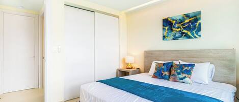 Une chambre à coucher avec un lit, une table de chevet, une lampe, un tableau et une armoire.