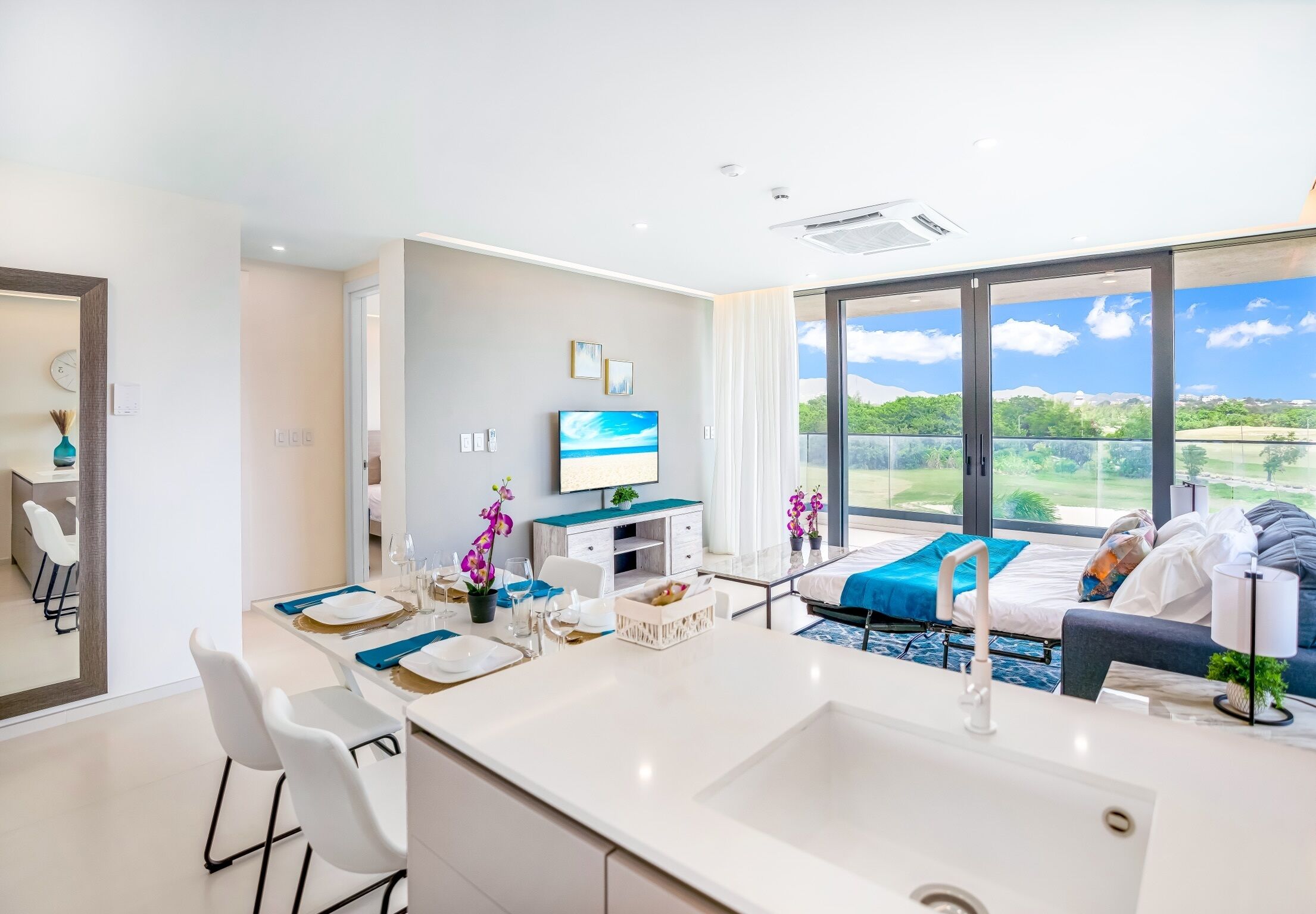 Ein modernes Hotelzimmer mit großem Balkon, einem Essbereich, einem Bett und einem Fernseher.
